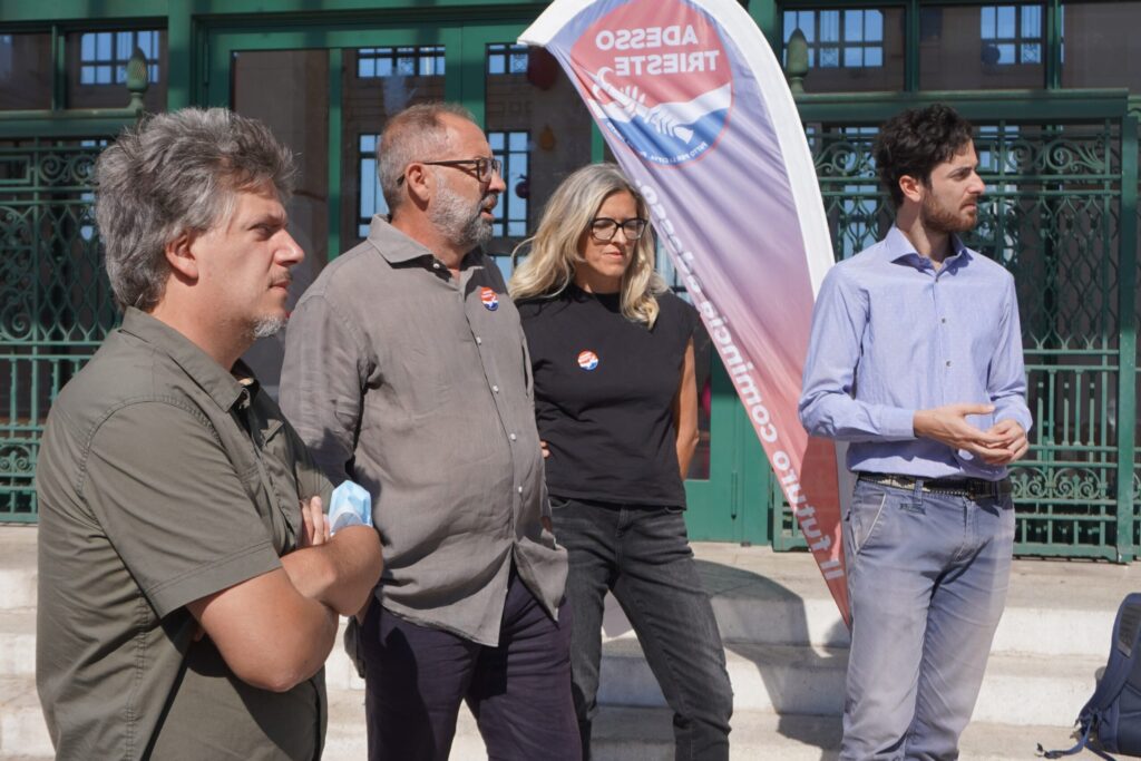 Quattro adulti in visita guidata all’aperto davanti a un edificio storico in città.