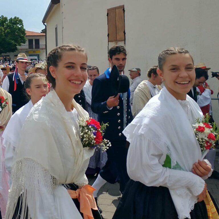 Due donne sorridenti in abiti tradizionali con fiori a una festa di paese.