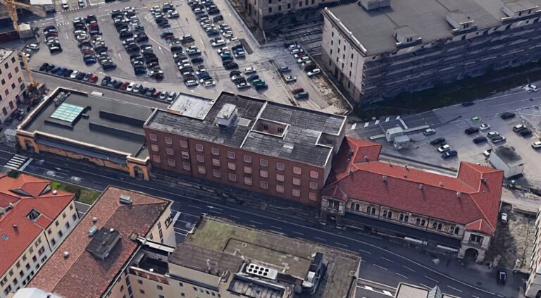 Veduta aerea di edificio in mattoni a Trieste con parcheggi e strade urbane.