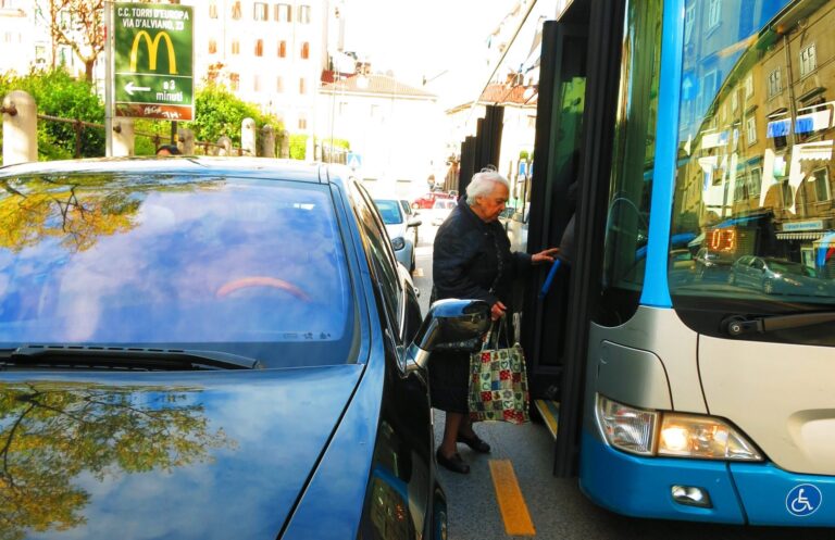 Anziano sale su bus a Trieste tra auto parcheggiata e marciapiede stretto.