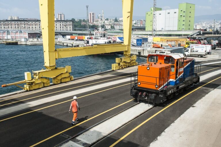 Locomotiva portuale a Trieste con operatore, gru container e nave nel terminal.