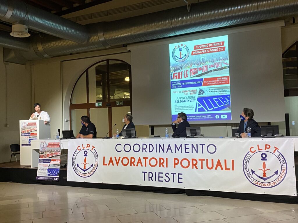 Assemblea CLPT dei lavoratori portuali di Trieste con relatori al tavolo e podio.