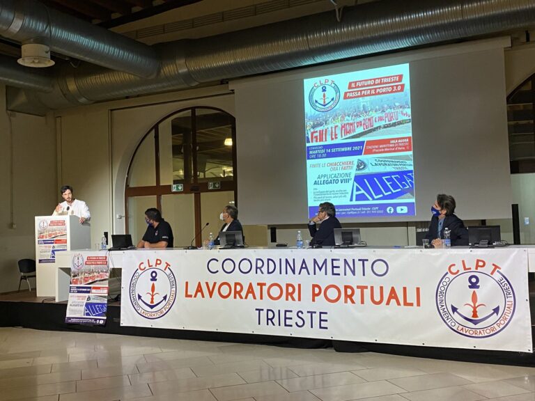 Assemblea CLPT dei lavoratori portuali di Trieste con relatori al tavolo e podio.