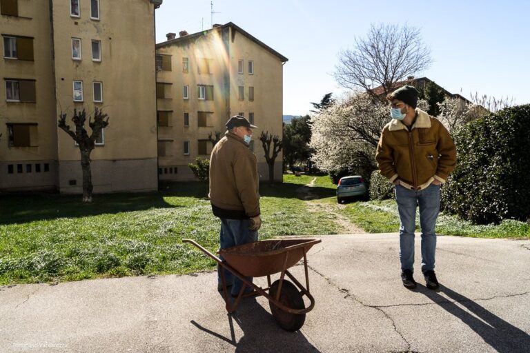 Due uomini con carriola rossa in cortile residenziale soleggiato.