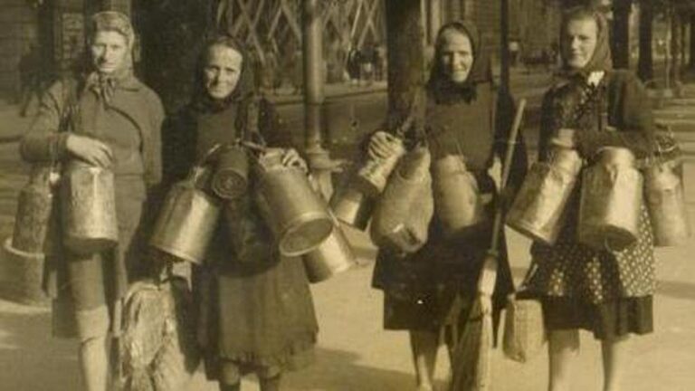 Quattro donne lavoratrici vintage con secchi e attrezzi in una scena storica all’aperto.