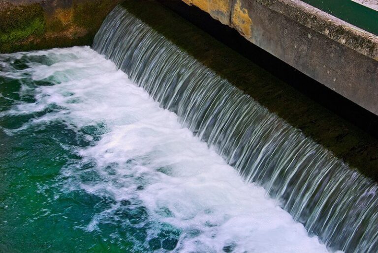 Acqua che cade su sfioratore in cemento con schiuma bianca e forte turbolenza.