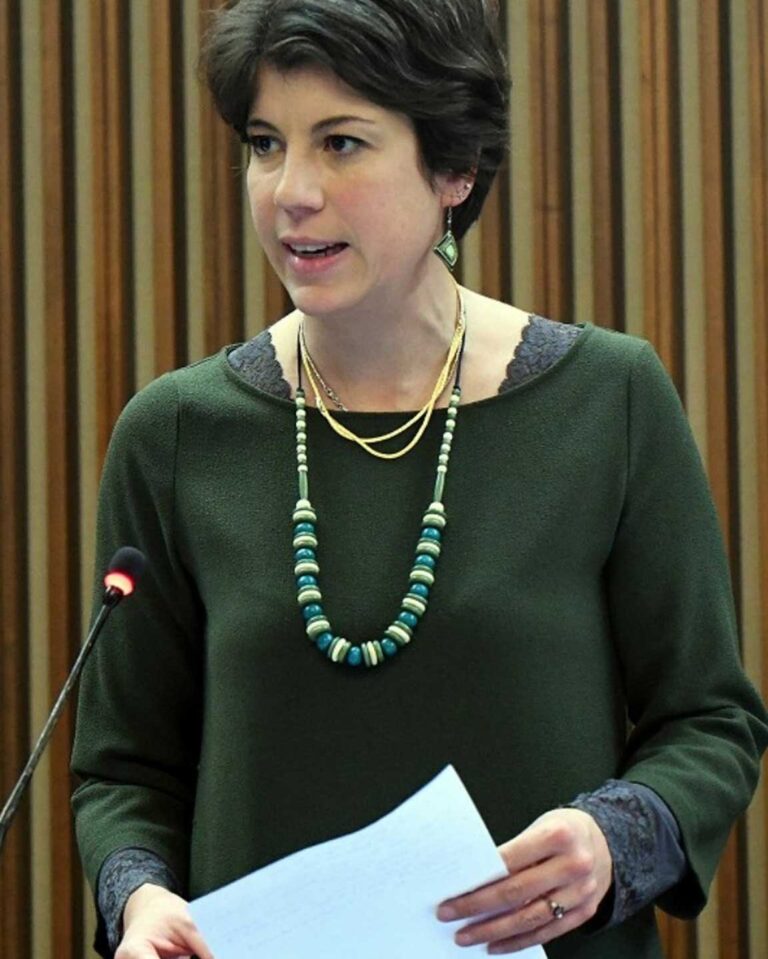 Donna parla in aula istituzionale con fogli in mano e microfono acceso.