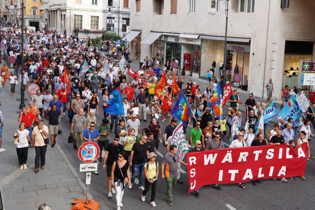 Corteo sindacale Wärtsilä a Trieste con striscione rosso e bandiere nel centro città.