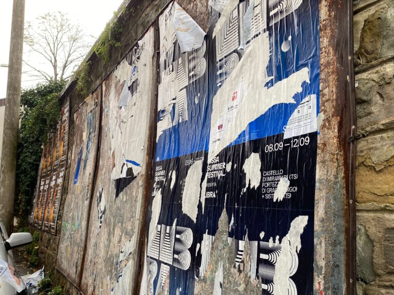 Muro urbano degradato con poster strappati, pietra grezza e scooter in vicolo.