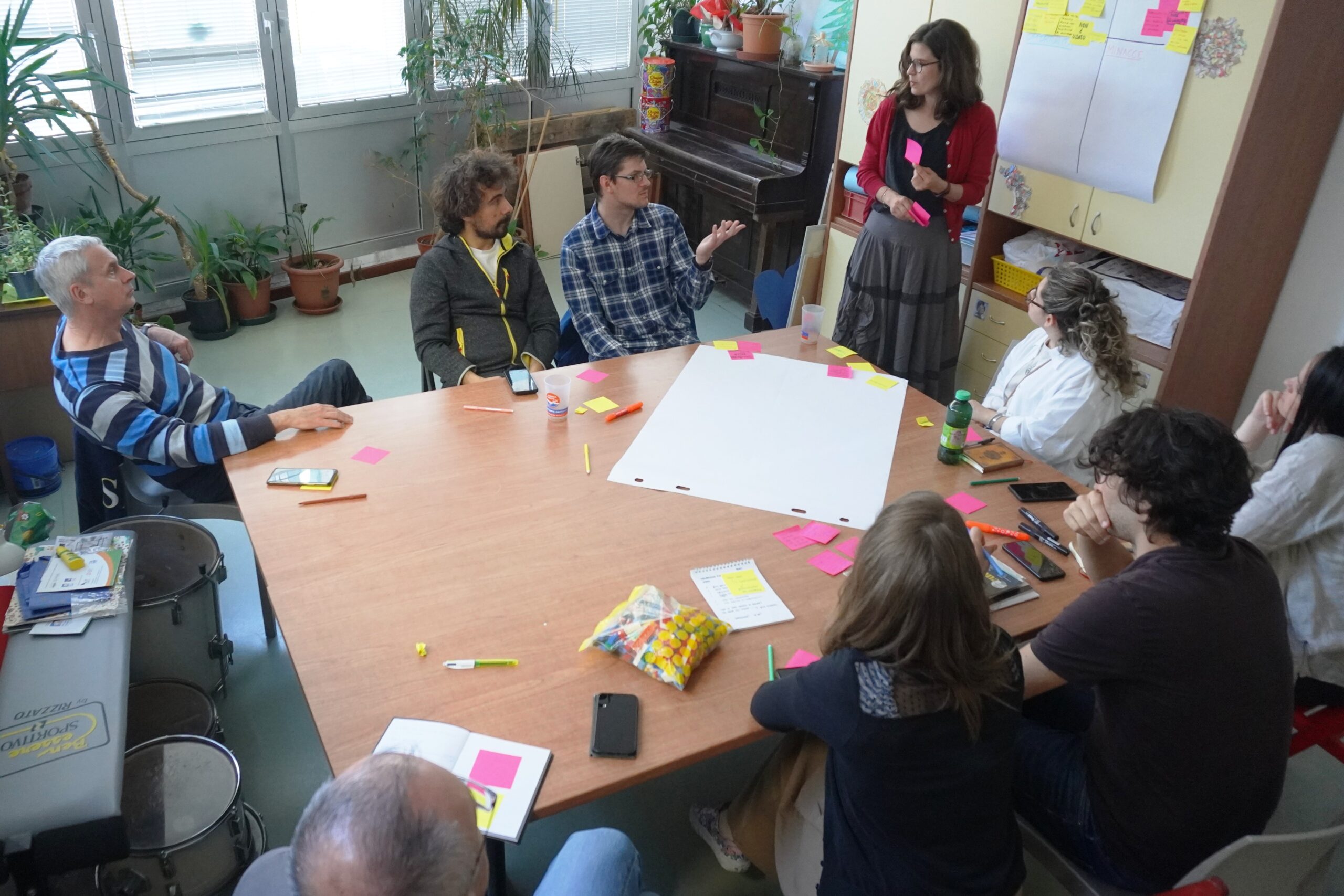 Gruppo di lavoro in cerchio, sala luminosa con facilitatrice, post-it e partecipanti attenti